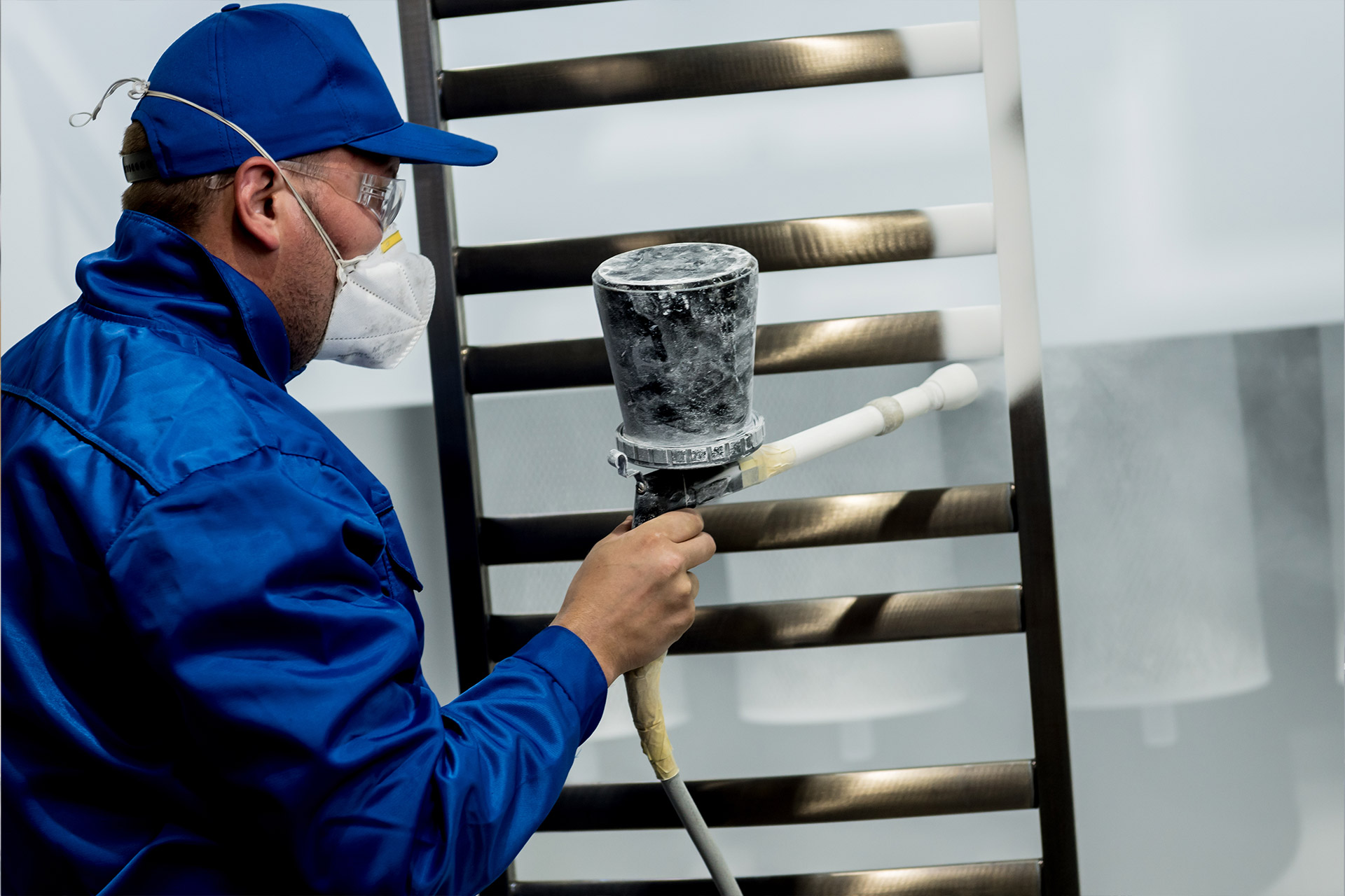 worker using a spray gun to disperse powder coating on metal bars